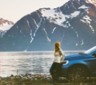 woman with car in front of a fjord and snow topped mountain